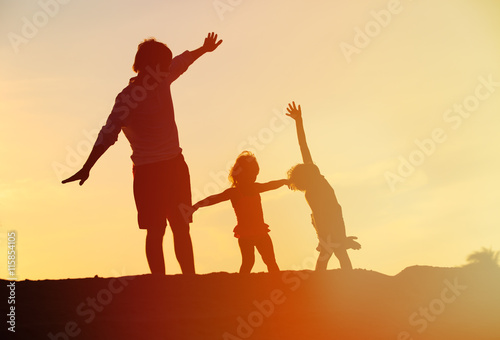 father with son and daughter silhouettes play at sunset