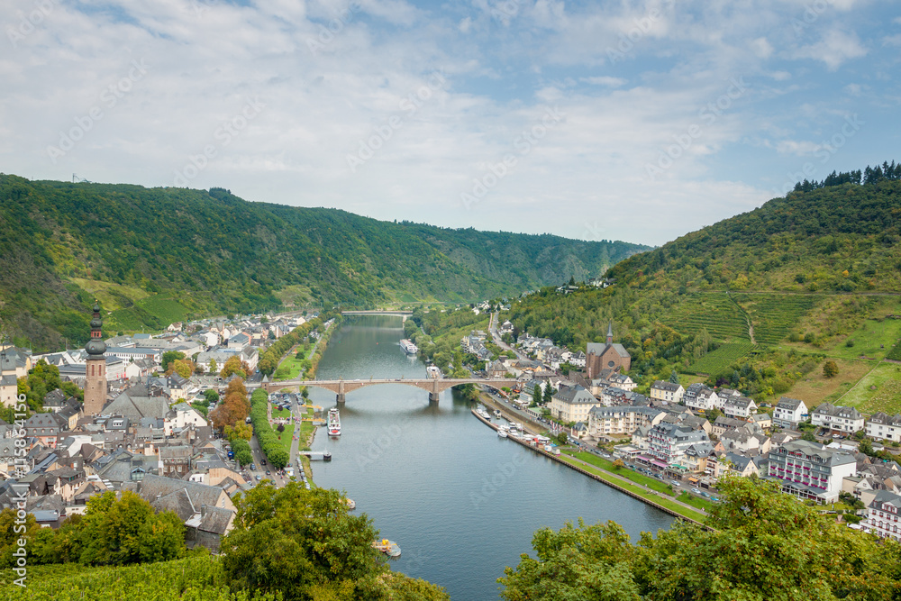 The picturesque German town of Cochem from above. Germany. Urban landscape with river and bridge. The town is surrounded by vineyards. Blue sky and white clouds. Old town.