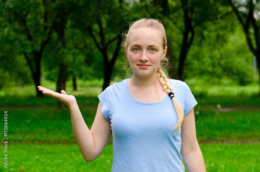 Portrait of happy surprised young pretty girl, showing something or blank copyspace area for slogan or text message, against green summer park background