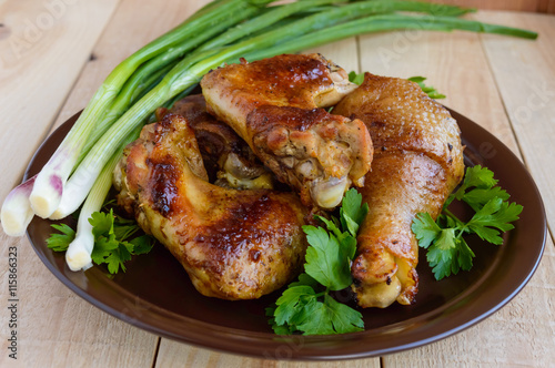 Roasted juicy chicken (legs, winglets) on a clay plate on a light wooden background