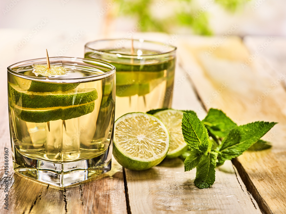 Alcohol drink. On wooden boards two glasses with alcohol green transparent drink. A drink number hundred sixty five mojito cocktail with half lime and mint . Country life style. Light background. Alcohol drink. On wooden boards two glasses with alcohol green transparent drink. A drink number hundred sixty five mojito cocktail with half lime and mint . Country life style. Light background.