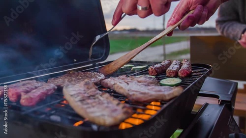 A senior man is slowly turning around meat on the barbecue grill. He and his wife are about to have some nice dinner. Close-up shot.
