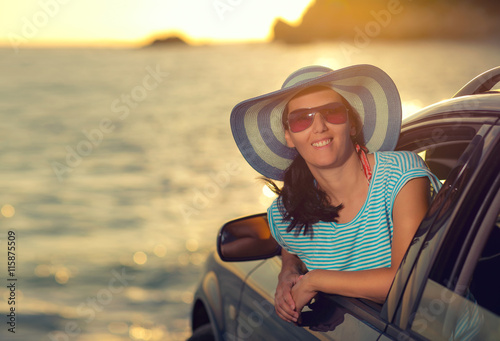 Relaxed happy woman on summer roadtrip travel vacation leaning out car window on sea and blue sky background, sunlight
