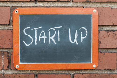 Tafel an einer Ziegelwand mit Text / Tafel an einer Ziegelwand mit Text START UP.