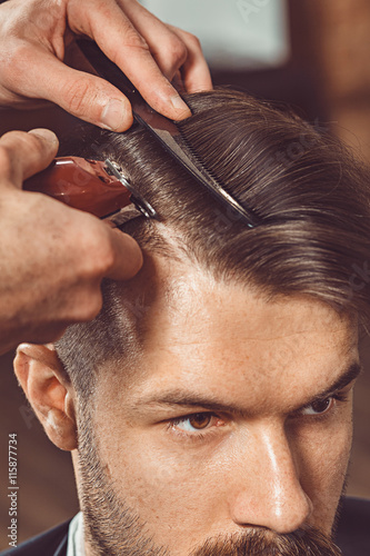 The hands of young barber making haircut to attractive man in barbershop Fotobehang