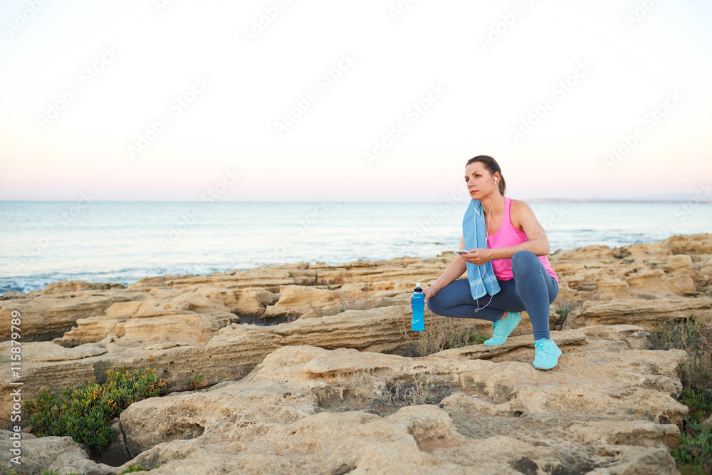 Woman sitting after morning running on the rocks by the sea