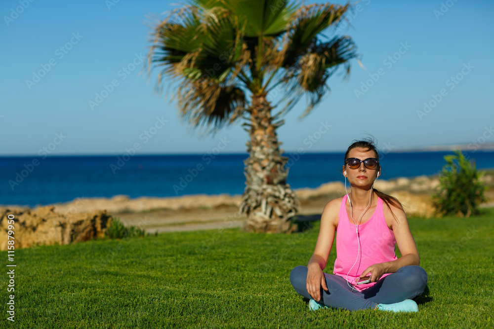 Sport girl meditates on the grass near the sea, practicing yoga