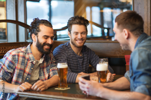 male friends with smartphone drinking beer at bar