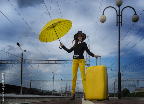 Young girl with a camera and a yellow suitcase waiting for a train