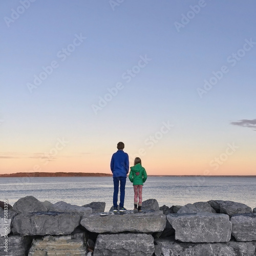 Boy and girl standing on rocks by sea, Asgardstrand, Norway photo