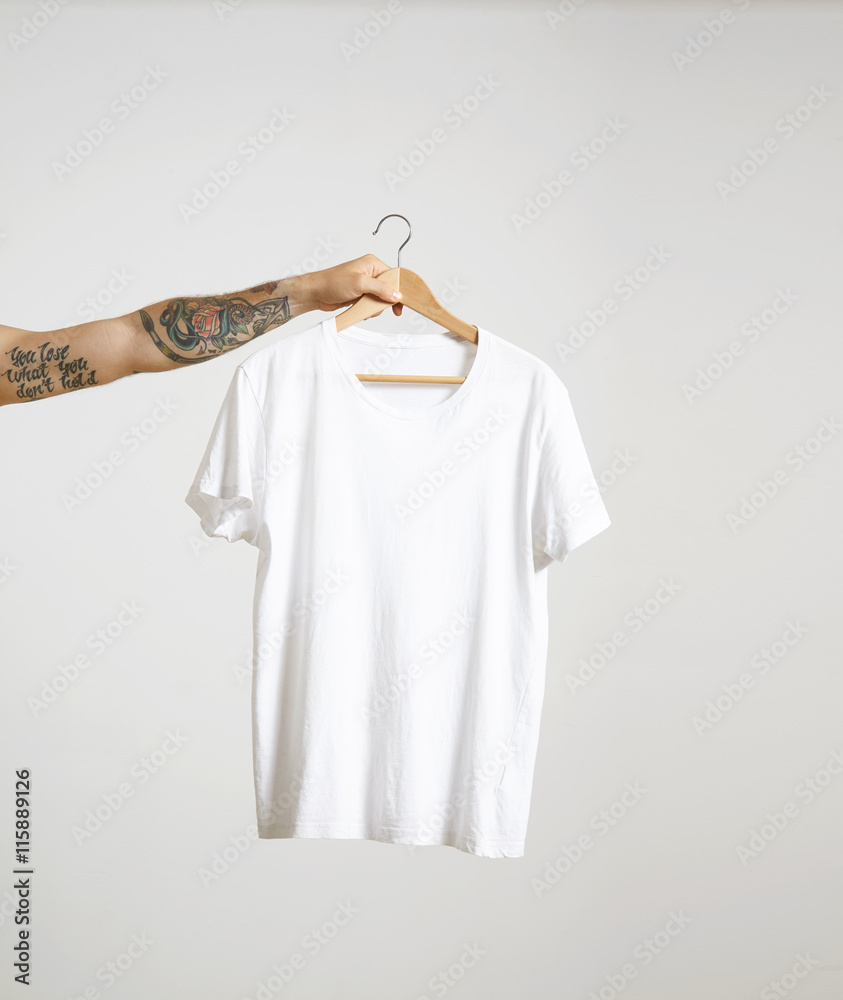 Tattooed biker hand holds hang with blank white t-shirt from premium thin  cotton, isolated on white mockup Stock-Foto | Adobe Stock
