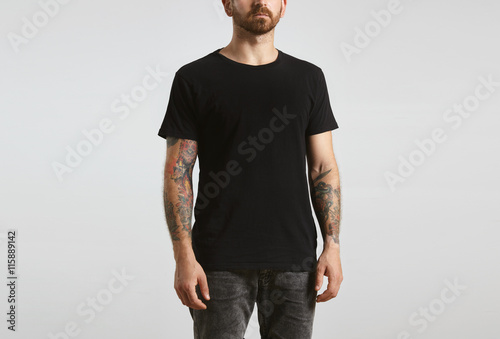 Brutal attractive bearded biker man with tattooed hands poses in black blank t-shirt from premium thin cotton, isolated on white mockup