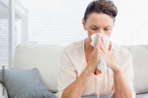 Mature woman suffering from cold while sitting on sofa