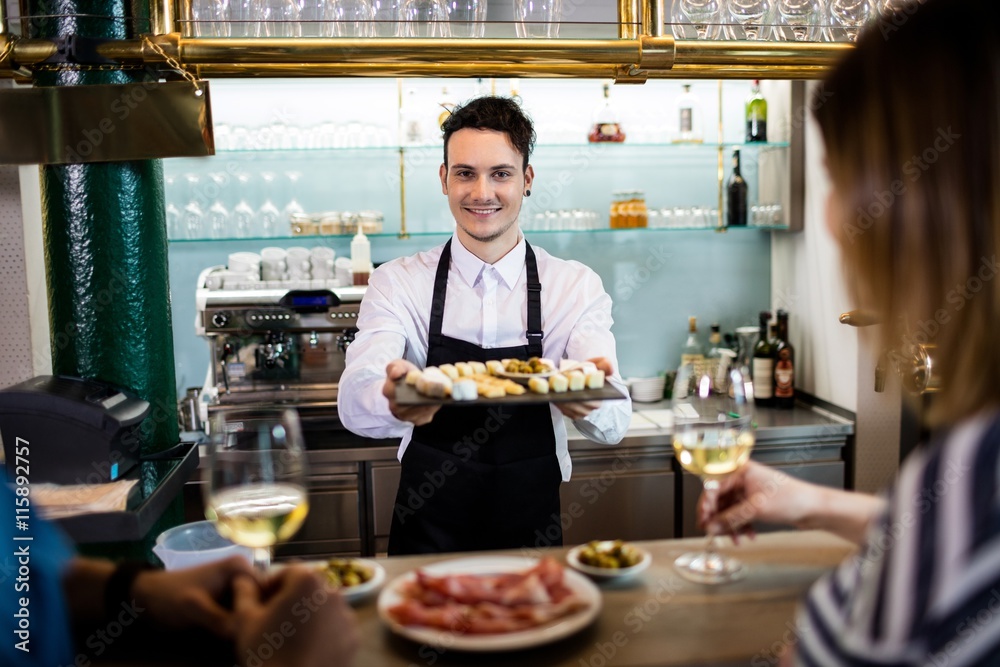 Young bartender serving food to customers at counter 