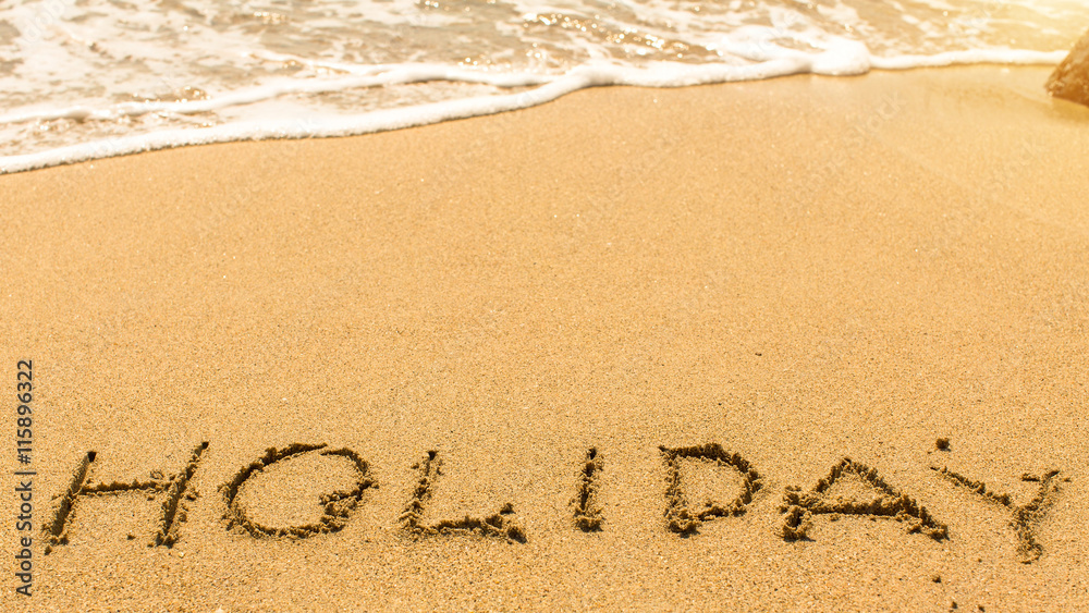 Holiday - hand-written on the sand in line of the sea surf.