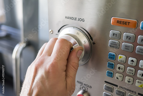 Man works with control panel CNC machine. Hand turns knob on control panel. 