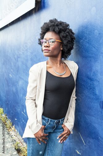 Young African woman standing on a blue wall in the background