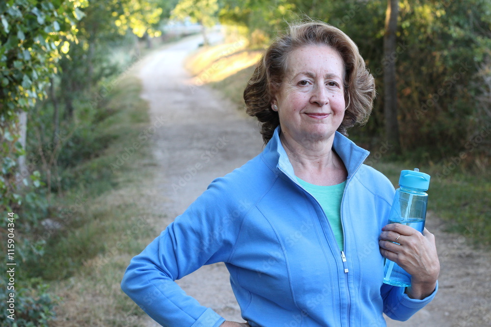 A gorgeous mature woman standing outdoors smiling holding a water bottle A gorgeous mature woman standing outdoors smiling holding a water bottle