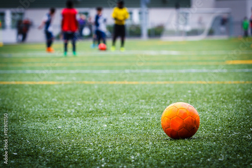 Dirty soccer ball on the artificial turf field with game in the background