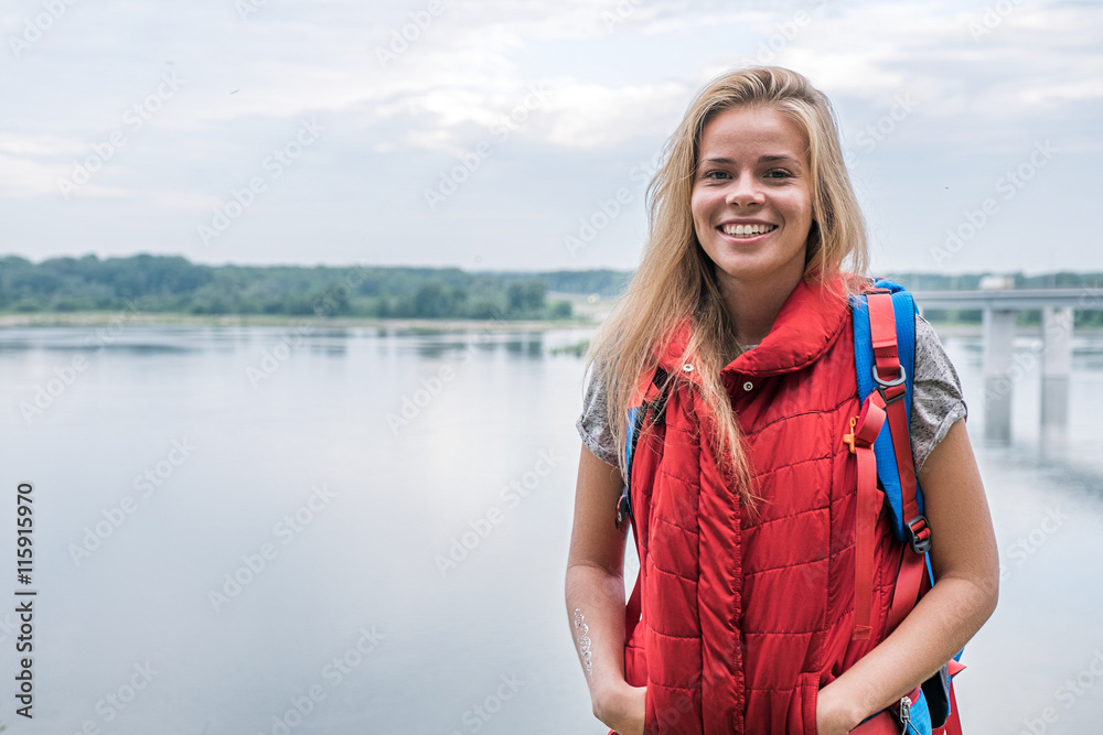 Happy blonde traveler smiling at camera against of river