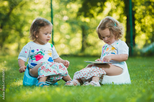 The two little baby girls sitting on pottys against green grass