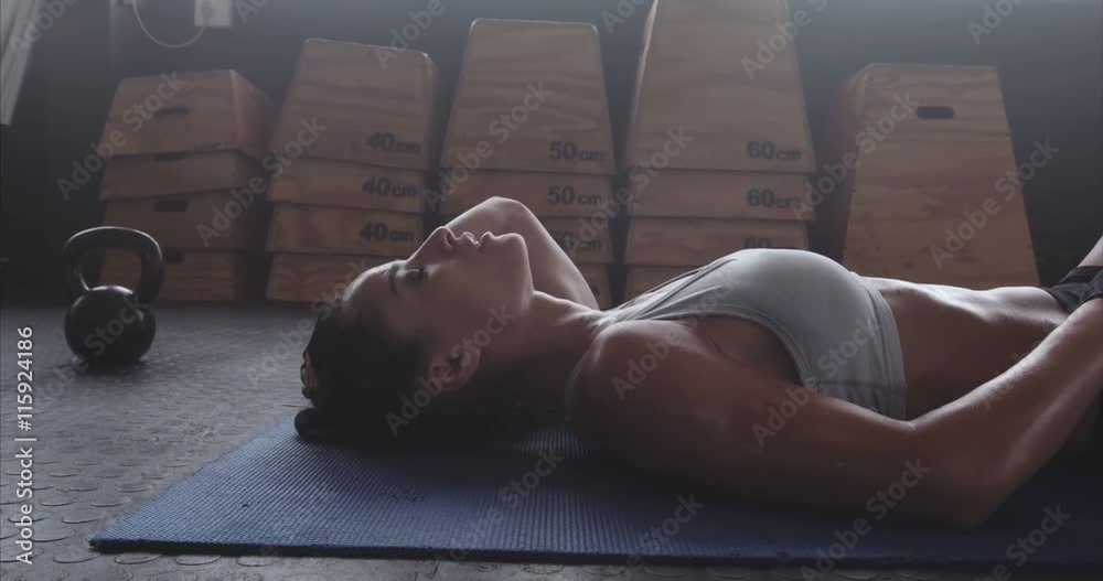 Sportswoman resting on exercise mat after intense fitness training at gym. Female athlete taking a break after cross fit exercise. Exhausted and sweaty muscular woman taking deep breath. 
