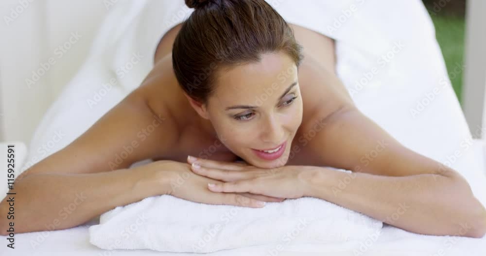 Woman smiles and relaxes on massage table on pleasant summer day in outdoor spa