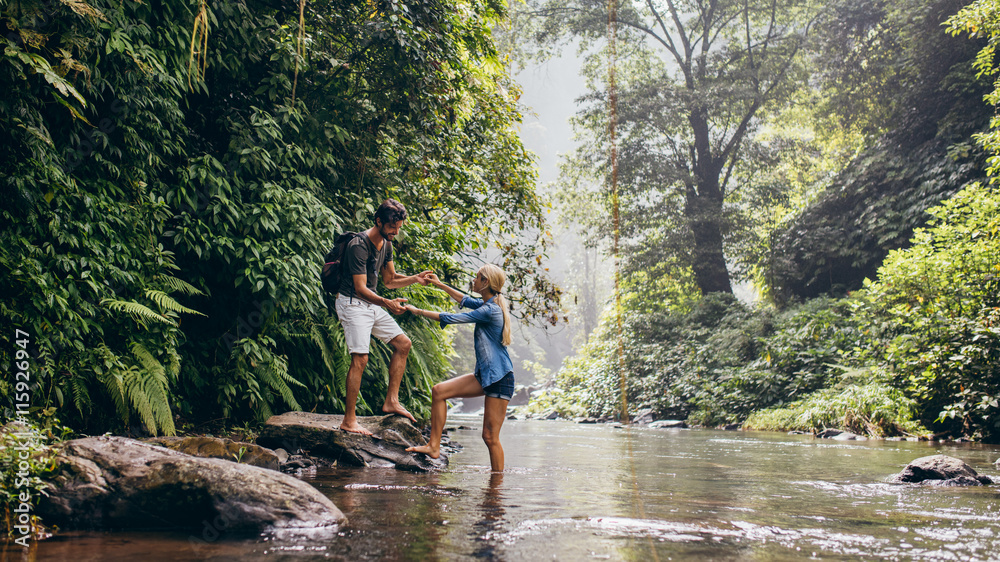 Man helping woman crossing stream Man helping woman crossing stream