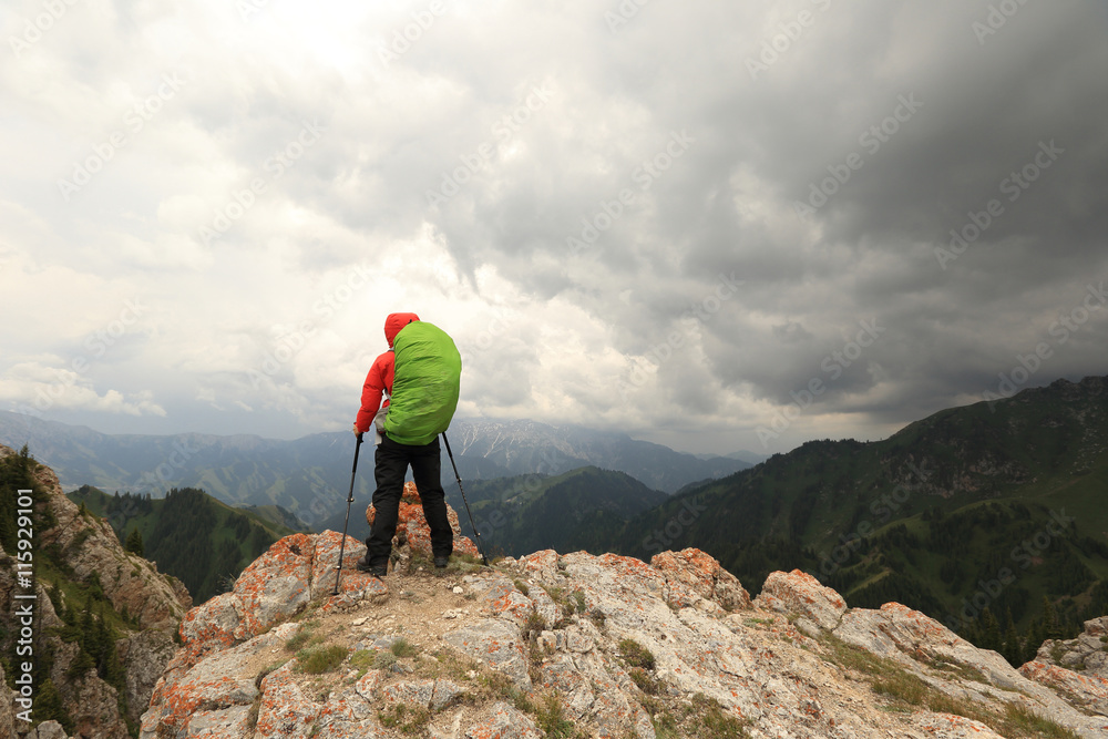 Obraz premium successful woman backpacker hiking on mountain peak cliff