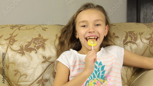 Girl licking candy on a stick in the form of lemon and and smiling