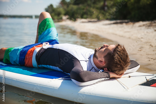Young man lies on paddle board on the beach