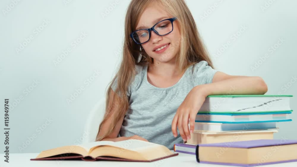 Portrait four-eyes schoolgirl 7-8 years reading book at the table on white background. Child smiling at camera Portrait four-eyes schoolgirl 7-8 years reading book at the table on white background. Child smiling at camera