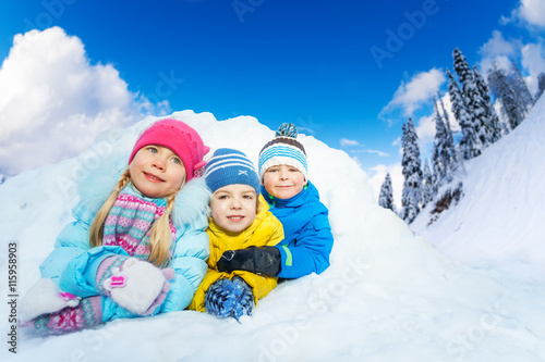 Three little kids smile from snow cave