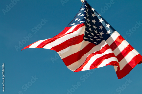 United States flag blows in the wind against a blue sky attached to the wall from the side.
