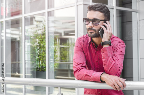 business man in a red shirt talking on a mobile phone outside of photo