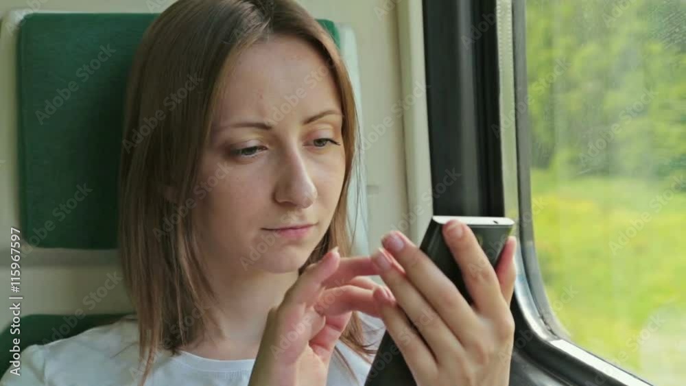 Young pretty woman sits near window and uses her mobile while traveling by train Young pretty woman sits near window and uses her mobile while traveling by train
