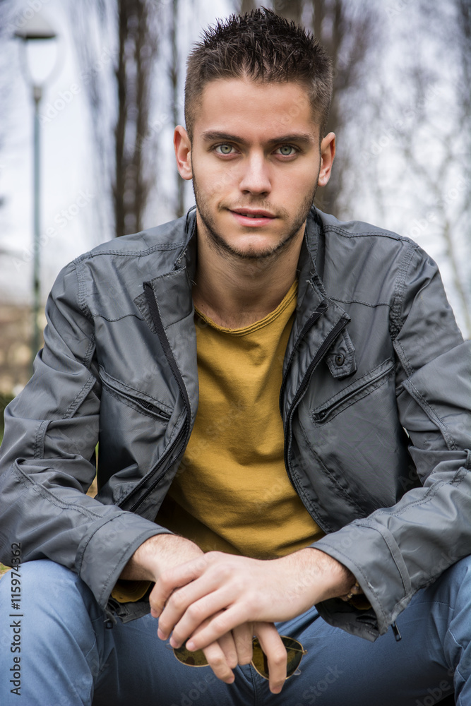 Portrait of handsome young man looking to a side while sitting in city park Portrait of handsome young man looking to a side while sitting in city park
