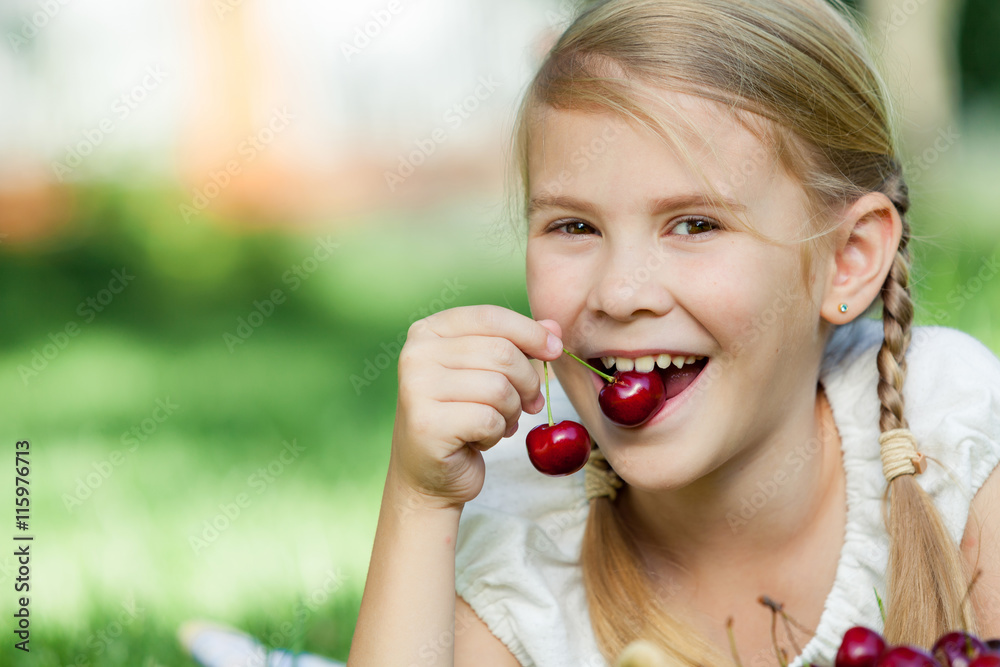 Happy little girl lying near the tree with a basket of cherries Happy little girl lying near the tree with a basket of cherries
