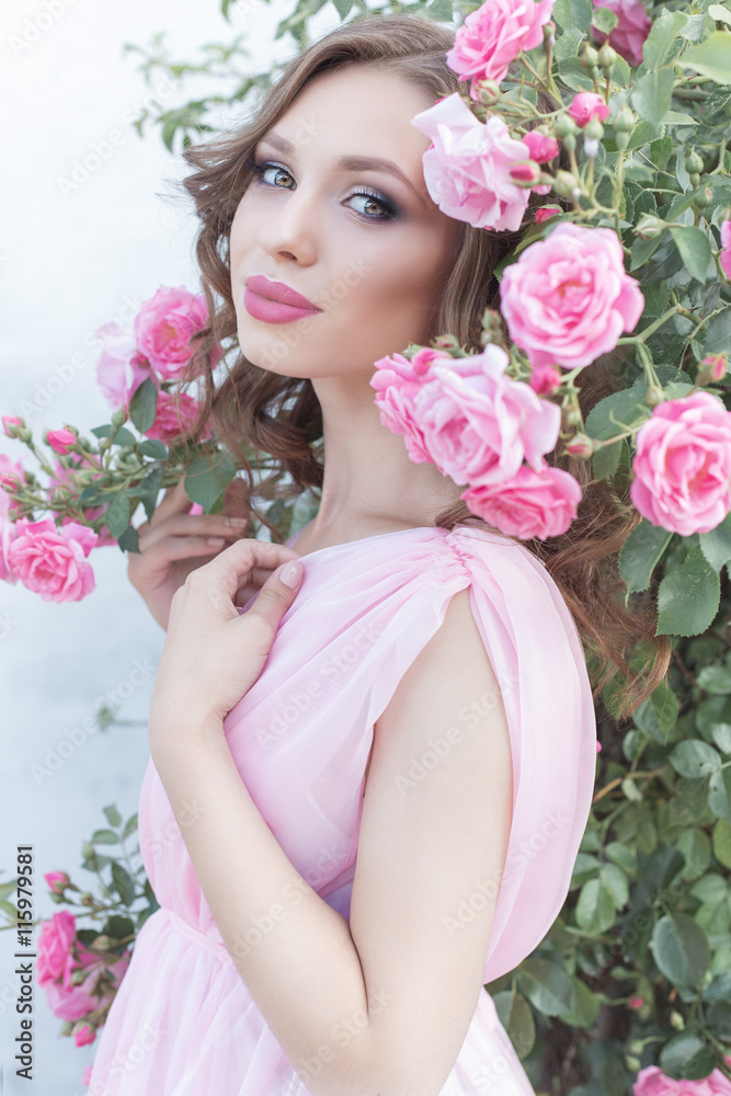 beautiful sexy girl in a pink dress standing in the garden roses in a sunny bright summer day with a gentle make-up and bright puffy big lips