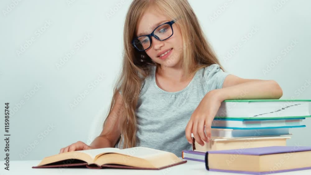 Close up portrait four-eyes 7-8 years reading book at the table isolated on white. Child smiling at camera Close up portrait four-eyes 7-8 years reading book at the table isolated on white. Child smiling at camera