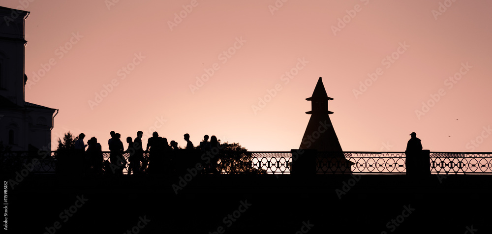 Silhouettes of people walking across bridge against the sky