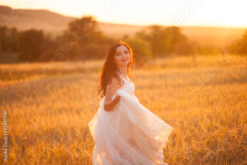 Happy beautiful young bride outside on a summer meadow at the sunset