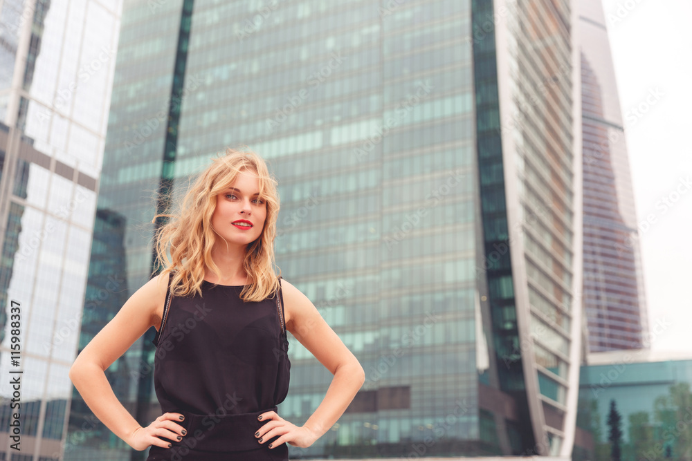 Fototapeta premium Beautiful smiling blonde lady in black dress outdoors