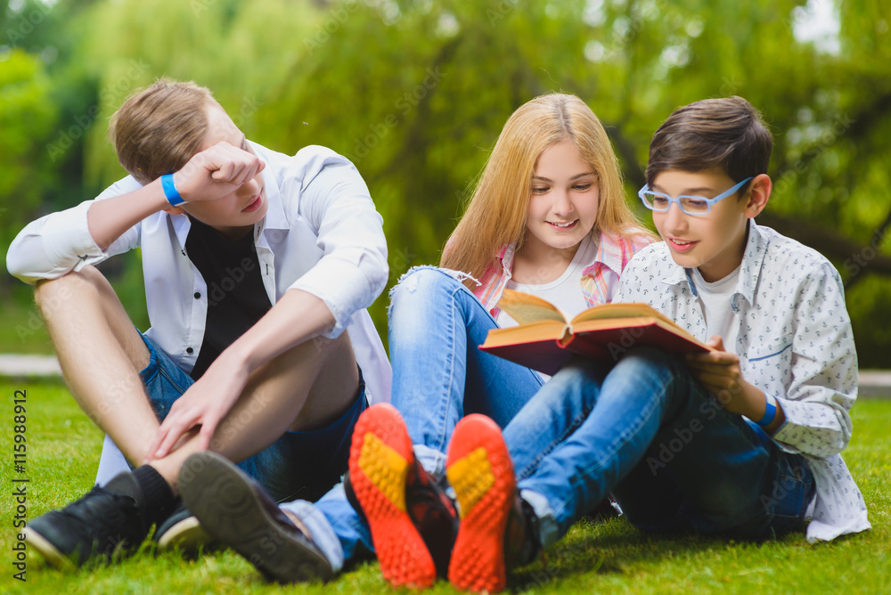 Smiling kids having fun and reading book at grass. Children playing outdoors in summer. teenagers communicate outdoor