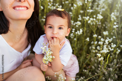 Smiling happy cute mother and daughter playing on a flower field and looking up, nautre background.