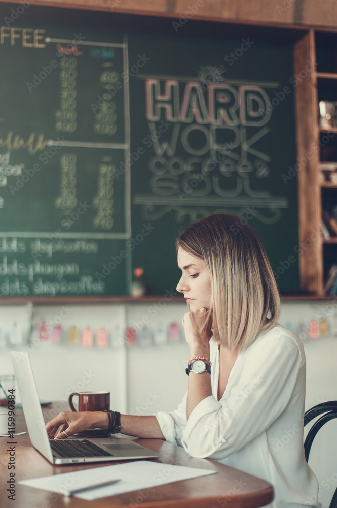 Fototapeta premium Young woman freelancer working with laptop in cafe