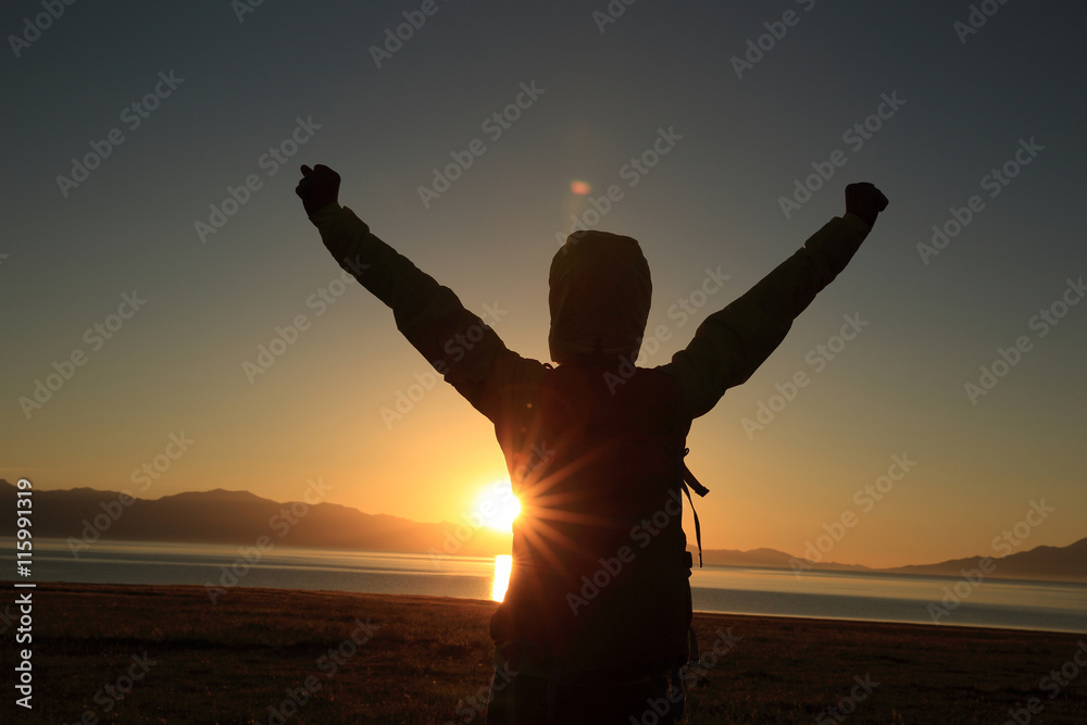 young woman hiker open arms under the sunrise at sea