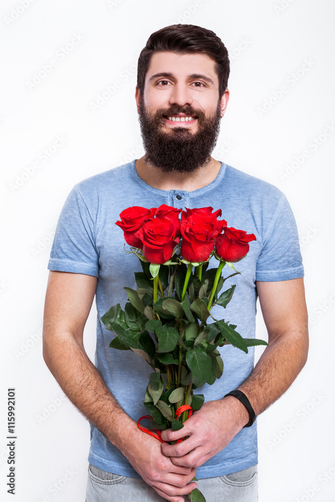 This is for you! Handsome young man holding bouquet with red roses while standing isolated on white background