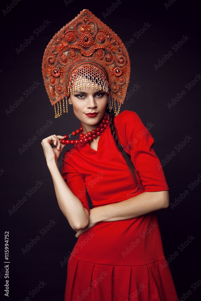 Fototapeta premium Beautiful woman in red dress posing in metal headwear on black background