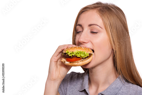 Guilty pleasures... Closeup of a young beautiful  woman eating a big hamburger  isolated on white background.